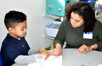 Volunteer parent, Kirstian Siddiq works with kindergartener Leo Weeks on a math problem.